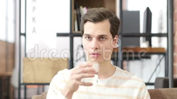 年轻人坐在家里的沙发上喝水看着摄像机视频的预览图