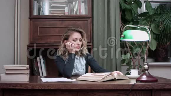 一位疲惫的年轻女子坐在桌子旁在书上睡着了视频的预览图