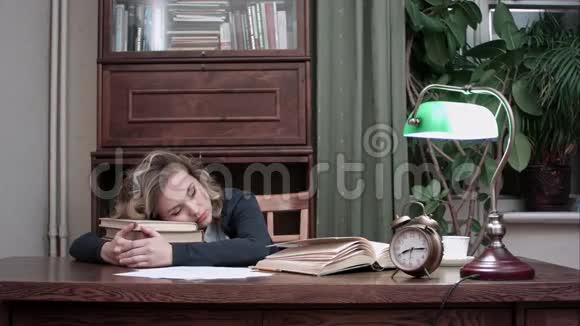 疲惫的女性在工作场所的一堆书上打盹被闹钟吵醒视频的预览图