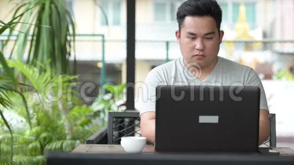 年轻英俊的超重亚洲男人在咖啡店放松视频的预览图