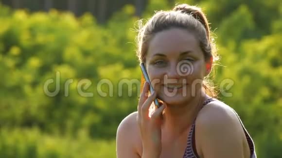 快乐的年轻女子坐在草地上用电话或智能电话交谈视频的预览图