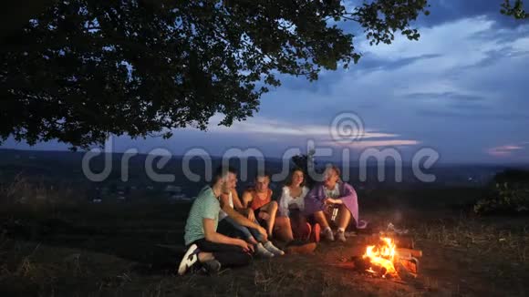 一群朋友坐在篝火旁喝着热饮料和交谈视频的预览图