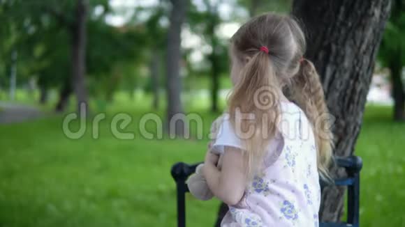 阴天里小女孩和一只玩具兔子坐在公园的长凳上视频的预览图