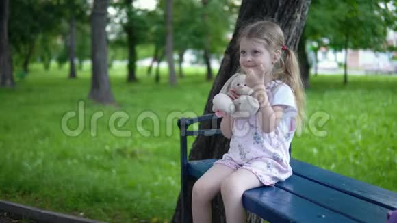 阴天里小女孩和一只玩具兔子坐在公园的长凳上视频的预览图