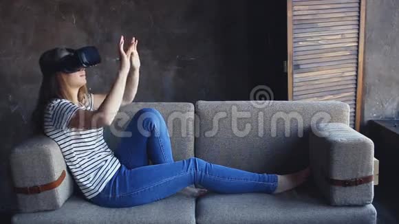 年轻女子坐在客厅的沙发上使用VR耳机视频的预览图