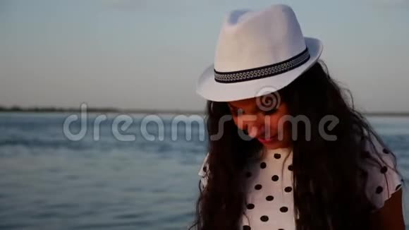 快乐的女孩戴着白色可爱的帽子沿着海边散步在沙滩上看着夕阳微笑着视频的预览图