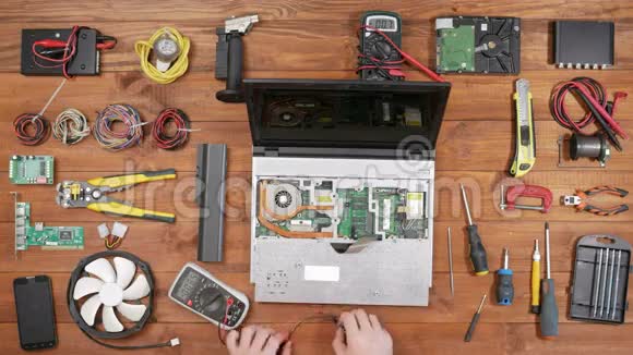 一个男人用万用表检查笔记本电脑的细节拆卸电脑一个木制桌面视图触摸一下视频的预览图