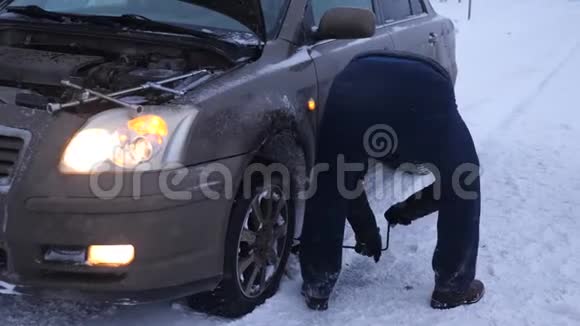 人在路上举起汽车千斤顶人类正在更换汽车车轮冬季在暴风雪中道路上更换车轮视频的预览图