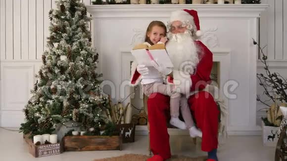 圣诞老人和可爱的女孩在圣诞树附近看书视频的预览图