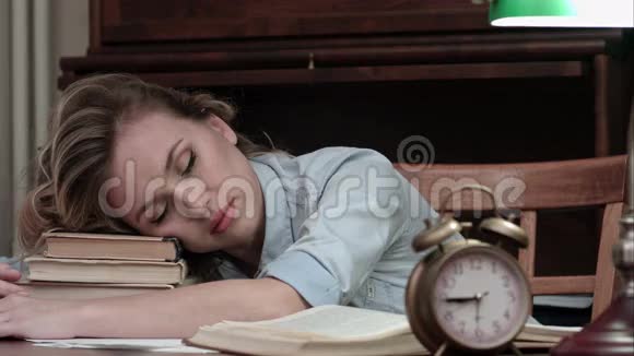 疲惫的女性在一堆书上打盹被闹钟吵醒视频的预览图