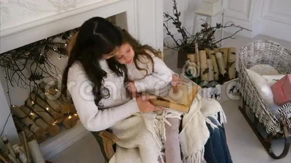 快乐的母亲和她美丽的女儿穿着白色毛衣在圣诞前夜看书视频的预览图