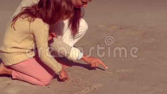 母亲和女儿在沙子上写作视频的预览图