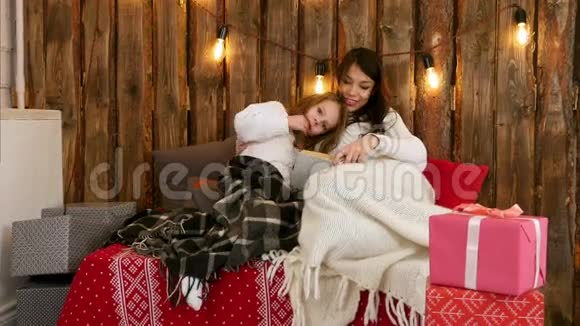 漂亮的年轻妈妈给她可爱的女儿读圣诞故事她坐在沙发上裹着毯子视频的预览图