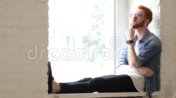 思考的设计师坐在窗边红头发和胡子视频的预览图