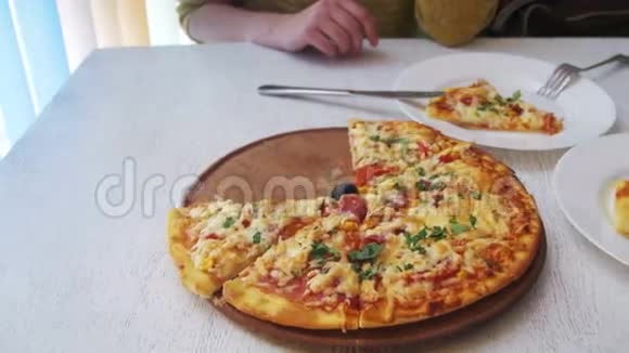 女孩正在吃一个比萨饼在一个白色的盘子在一个餐厅在一个白色的木制桌子多利射击视频的预览图