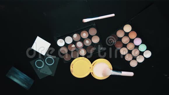 纹身女性的手使用化妆刷米色粉扑盒在黑色桌子上视频的预览图