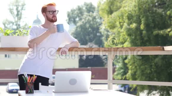 站在阳台室外思考一个勇敢的年轻人喝着咖啡视频的预览图