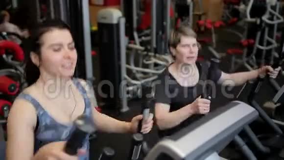 两个女人在健身房里使用运动机一群女人女孩在窗户上做运动体育运动健身房视频的预览图