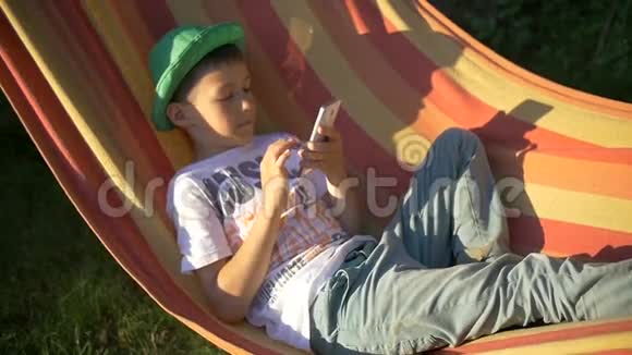 小男孩躺在吊床上看着他的手机放松下来视频的预览图