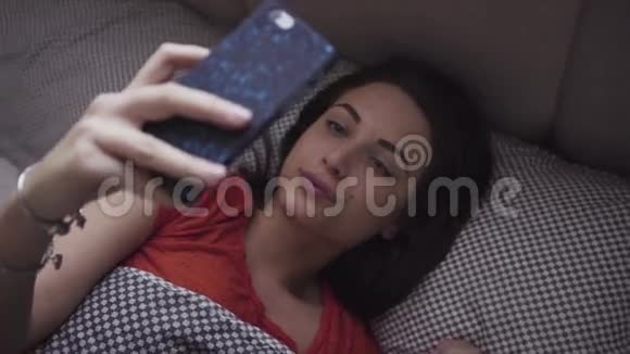 年轻的女人躺在床上用她的移动设备女孩看着智能手机屏幕对某件事做出反应视频的预览图