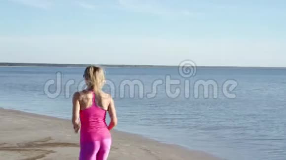 在阳光明媚的海滨背景下独立的年轻女子运动员在海滩上跑步运动女子跑步者短跑训练视频的预览图
