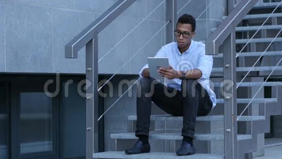 年轻黑人坐在楼梯上浏览平板电脑视频的预览图