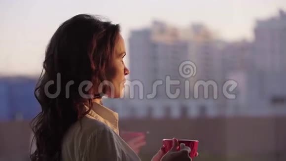 年轻漂亮的女商人欣赏城市风景在日落时分喝茶在现代办公室喝茶视频的预览图