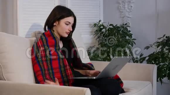 年轻女子坐在客厅的沙发上用手提电脑喝咖啡视频的预览图
