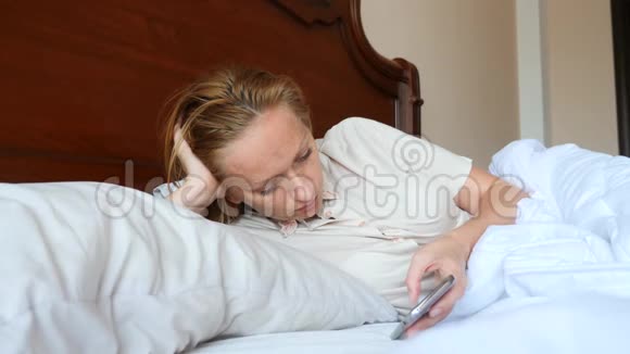 这位女士躺在床上使用智能手机4k慢动作视频的预览图