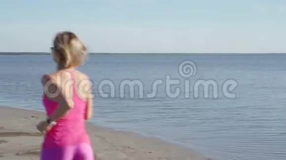 在阳光明媚的海滨背景下独立的年轻女子运动员在海滩上跑步运动女子跑步者短跑训练视频的预览图