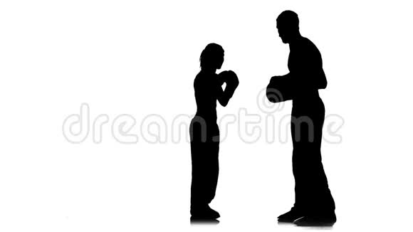 拳击手在拳击爪子上踢球女孩用脚在男孩手上踢球剪影白色背景视频的预览图