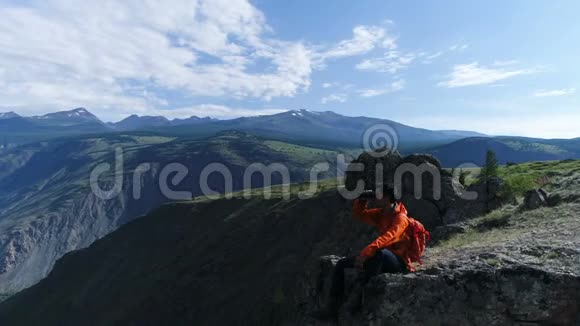 徒步旅行者站在山顶通过望远镜空中慢动作欣赏风景视频的预览图