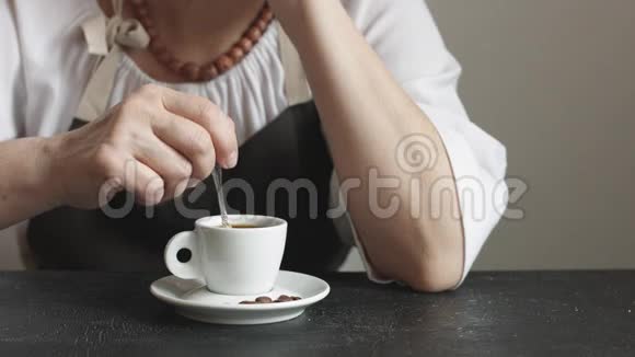 围裙里的女人在小杯热咖啡里搅拌糖视频的预览图