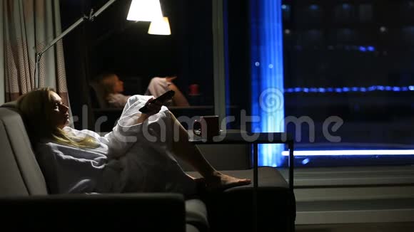 一个女人躺在沙发上手里拿着一个杯子靠近窗户可以看到城市的夜景看电视视频的预览图