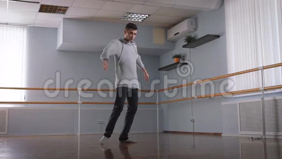 穿着灰色套头衫和黑色裤子的英俊的男舞者在教室的中央跳舞年轻的舞蹈学生视频的预览图
