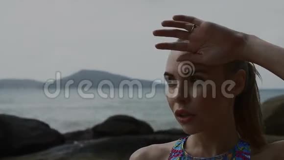 夏天一个漂亮的金发女人在训练后在海边的岩石间休息视频的预览图