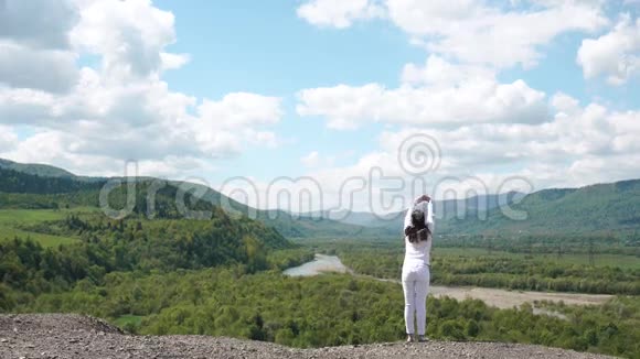 年轻女子站在山的边缘在壮丽的晴空下伸展身体视频的预览图