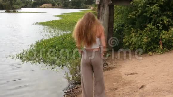 白种人少女站在泥河畔裤子和长发上视频的预览图