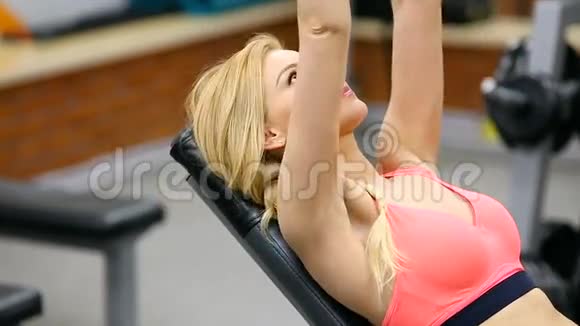 年轻女子在健身房用哑铃按着长凳练习三头肌和胸部视频的预览图