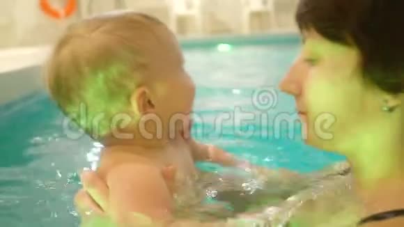 一位年轻的母亲带着一个小男孩游泳在游泳池里玩得很开心快乐的小男孩和他一起在游泳池里游泳视频的预览图