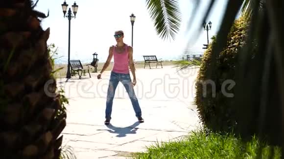 一个年轻快乐的家伙跳着现代芭蕾在海边的背景下摇摇晃晃地走着缓行视频的预览图