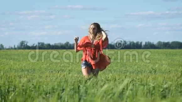 一个美丽的金发年轻幸福的女人穿着红色衬衫在绿色的田野上慢慢地走着视频的预览图