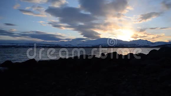 在雪山岛上的景色和北极圈峡湾表面的五颜六色的倒影上深深的生机勃勃的日落视频的预览图