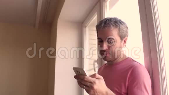 帅哥穿着粉红色T恤滚动应用程序在他的智能手机4K关闭Stealam视频视频的预览图