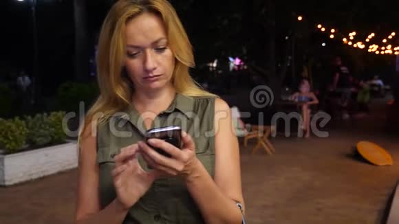 夏天一个金发女人在黑暗中在智能手机上键入一条短信晚上晚上4k慢动作视频的预览图