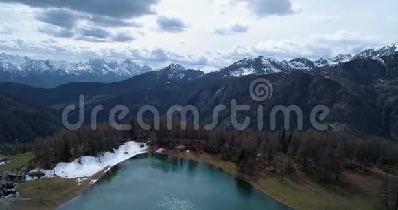 秋天在村庄和蓝湖之上向松松落叶林和雪山前进秋季阿尔卑斯山户外视频的预览图