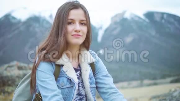 年轻的女旅行者坐在岩石上欣赏着山景微笑着看着相机视频的预览图