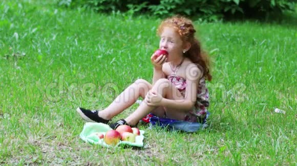 红头发的小女孩在草坪上吃苹果视频的预览图