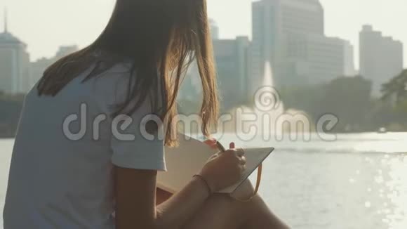 年轻女子坐在公园的长凳上写日记特写视频的预览图