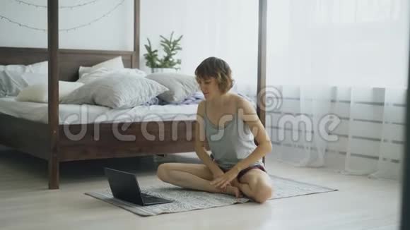 年轻有魅力的女人在家里做瑜伽运动在笔记本电脑上看教程视频的预览图